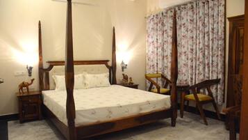 A four-poster bed with a floral bedspread, two bedside tables with lamps, a chair with a cushion, and a floral curtain.
