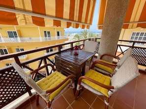 A balcony with wicker chairs and a wooden table, overlooking a building with balconies and a view of palm trees. - Edificio Don Antonio (Arona)