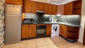A kitchen with wooden cabinets, a refrigerator, microwave, oven, dishwasher, and a washing machine. - Edificio Don Antonio (Arona)
