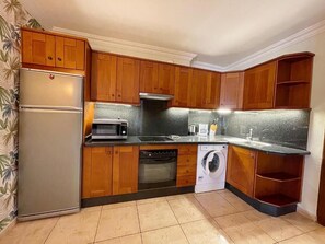 Eine Küche mit Holzausstattung, inklusive Kühlschrank, Mikrowelle, Backofen, Geschirrspüler und Waschmaschine.