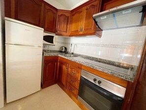 A kitchen with wooden cabinets, a white refrigerator, a microwave, a stove, and a tiled backsplash. - Edificio Don Antonio (Arona)