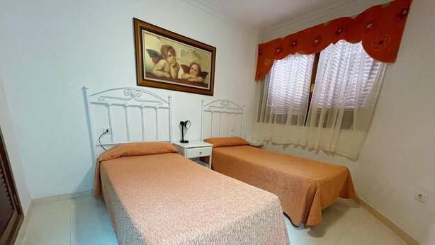 A bedroom with two beds, a nightstand, a mirror, a framed picture on the wall, and a window with curtains. - Edificio Don Antonio (Arona)