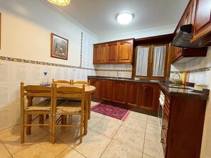 Una cocina con armarios de madera, una mesa de comedor con sillas y piso de baldosas.