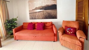 A living room with a sofa and armchair, a painting on the wall, and a plant. - Edificio Don Antonio (Arona)