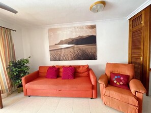 Ein Wohnzimmer mit Sofa und Sesseln, einem Gemälde an der Wand und einer Pflanze.