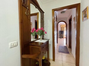 A hallway with a wooden desk, a mirror, and a vase with pink flowers. - Edificio Don Antonio (Arona)