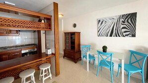 A kitchen with a wooden bar, white stools, a dining table with blue chairs, and a zebra print artwork on the wall. - Edificio Don Antonio (Arona)