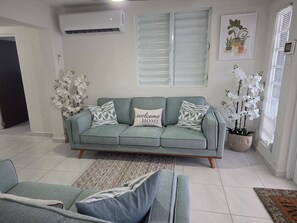 A living room with a grey sofa, patterned cushions, and a welcome home pillow.