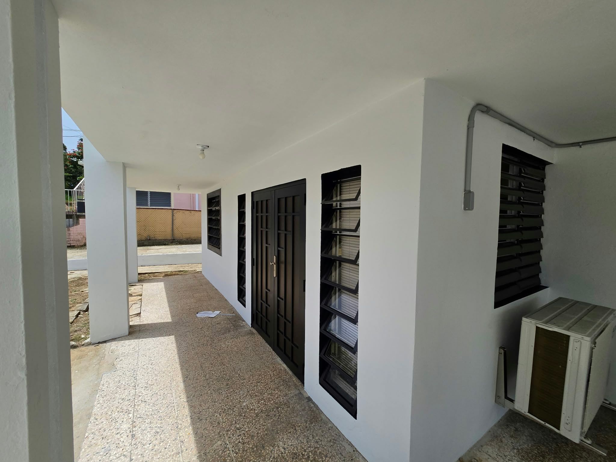 A corridor with multiple black-framed windows and a white air conditioning unit.