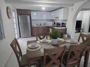 A dining area with a wooden table set for six, surrounded by chairs. A potted plant is on the table. - Perfect 4-bedroom house with AC in charming Humacao (Humacao)
