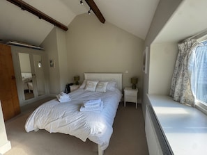 A bedroom with a large bed, a bedside table with a lamp, a radiator, a window with curtains, and a wardrobe with a mirror. - Lakeside Retreat A Romantic Country Escape (Whitchurch)
