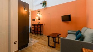 A modern living space with a sofa, a small table, and a TV mounted on the wall. - Nea Santa Monica By Dimorra  (Naples)