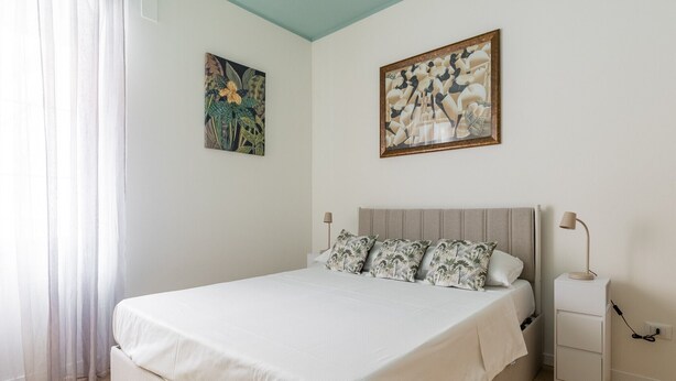 Un dormitorio con una cama, una mesita de noche, una lámpara y dos cuadros colgados en la pared.