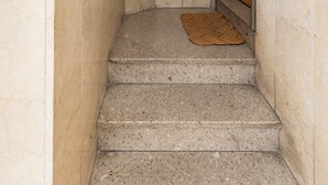 Una escalera estrecha con una puerta de madera arriba, un felpudo y una lámpara fijada a la pared.