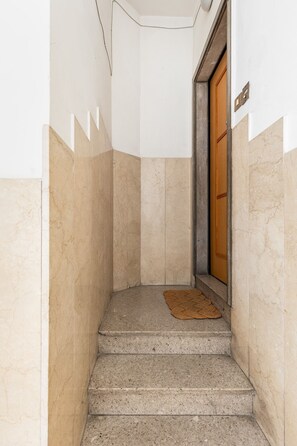 A narrow stairway with a wooden door at the top, a doormat, and a wall-mounted light fixture. - Casa 3 Frecce a Corte Isolani by Wonderful Italy (Bologna)