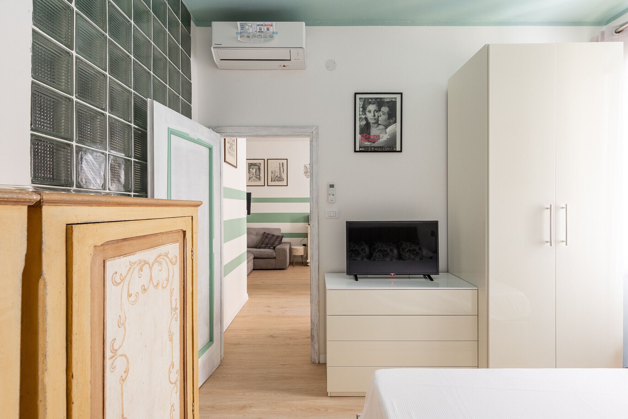 A room with a bed, a TV, a wardrobe, and a door leading to another room.