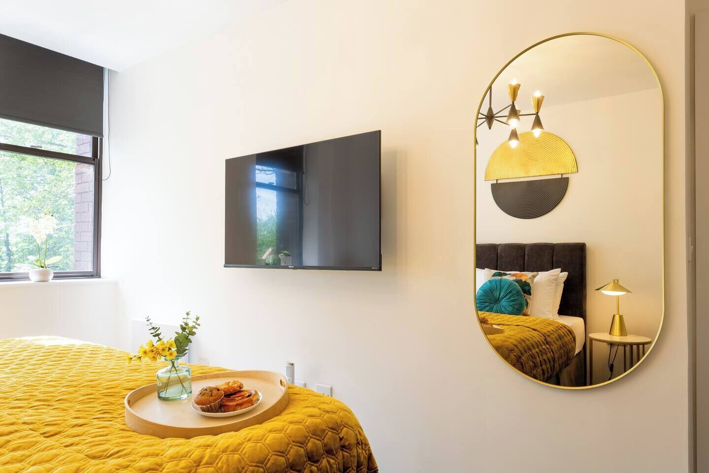 Ein Hotelzimmer mit einem Bett, einem runden Spiegel, einem Flachbildfernseher und einem Fenster mit Blick auf Grünflächen.