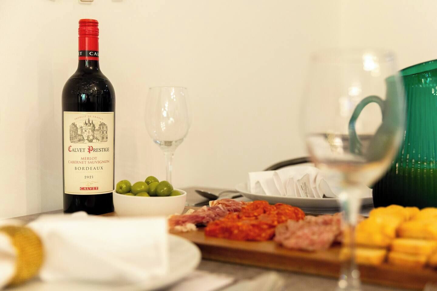 A bottle of Calvet Prestige Merlot, a glass of white wine, and a plate with food and olives.