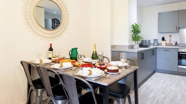 Un'area pranzo con uno specchio rotondo, un tavolo apparecchiato per un pasto e una cucina sullo sfondo.