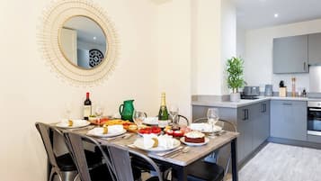 A dining area with a round mirror, a table set for a meal, and a kitchen in the background.
