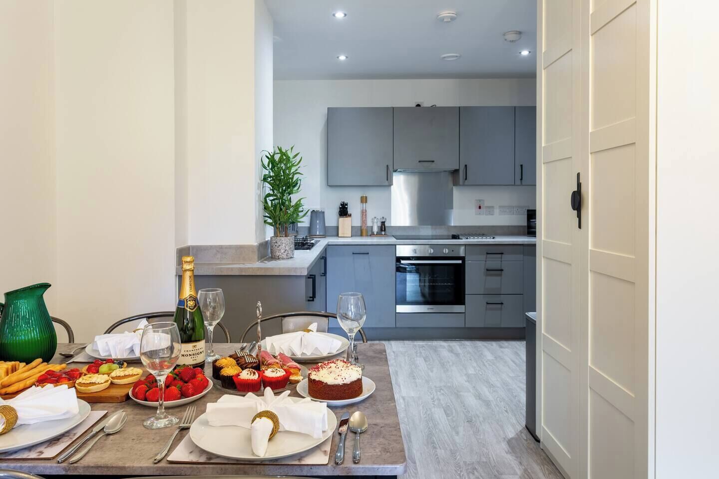 A modern kitchen with grey cabinets, a stainless steel oven, and a dining area with a table set for a meal.
