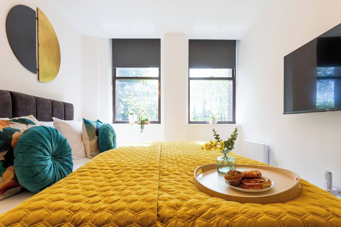 Ein modernes Schlafzimmer mit einem großen Bett, einem Fernseher und einem Fenster mit Blick auf Bäume.