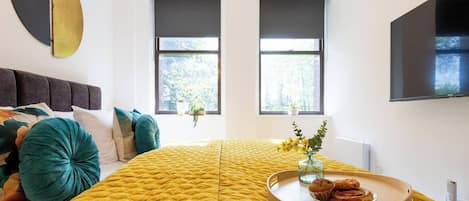 Ein modernes Schlafzimmer mit einem großen Bett, einem Fernseher und einem Fenster mit Blick auf Bäume.