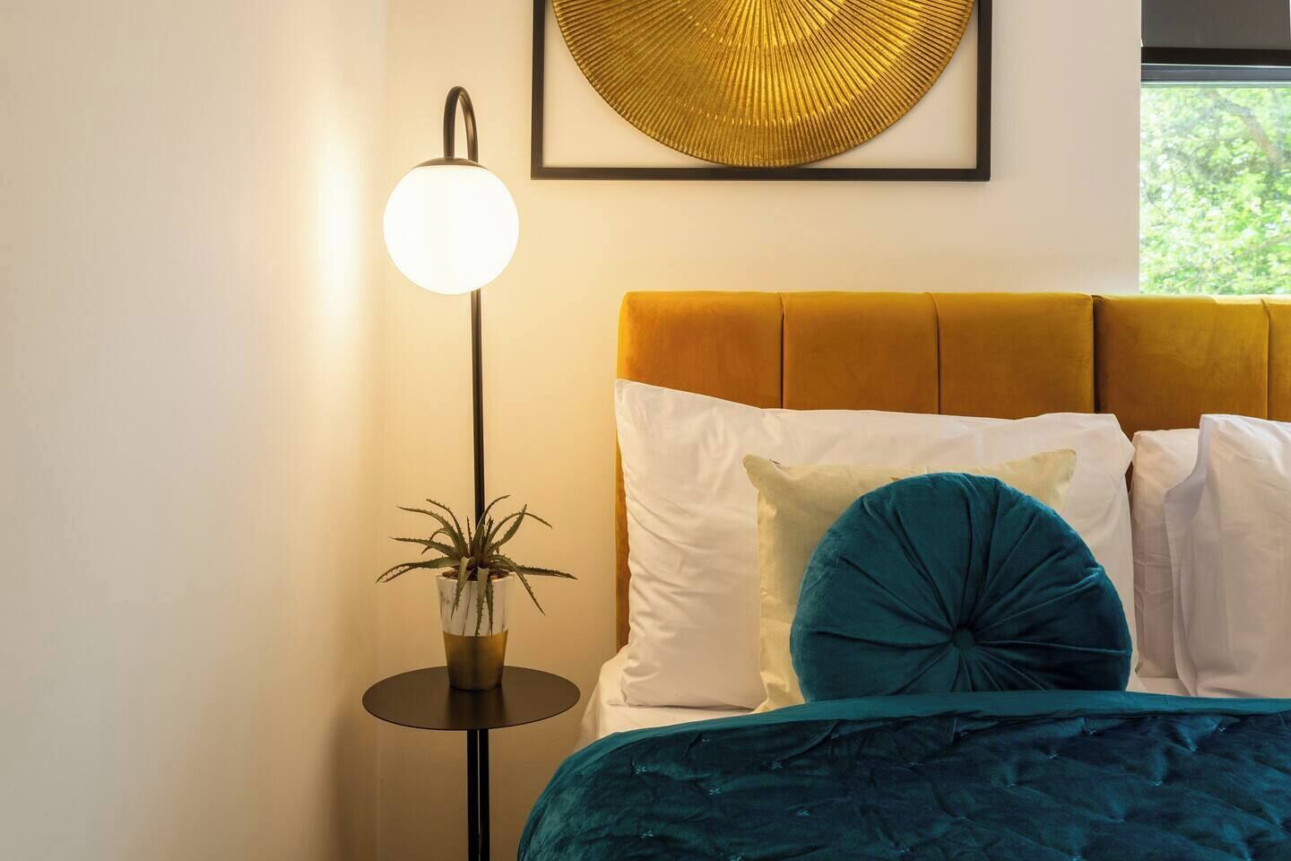 A bedroom with a bed, pillows, a bedside lamp, and a wall-mounted artwork.