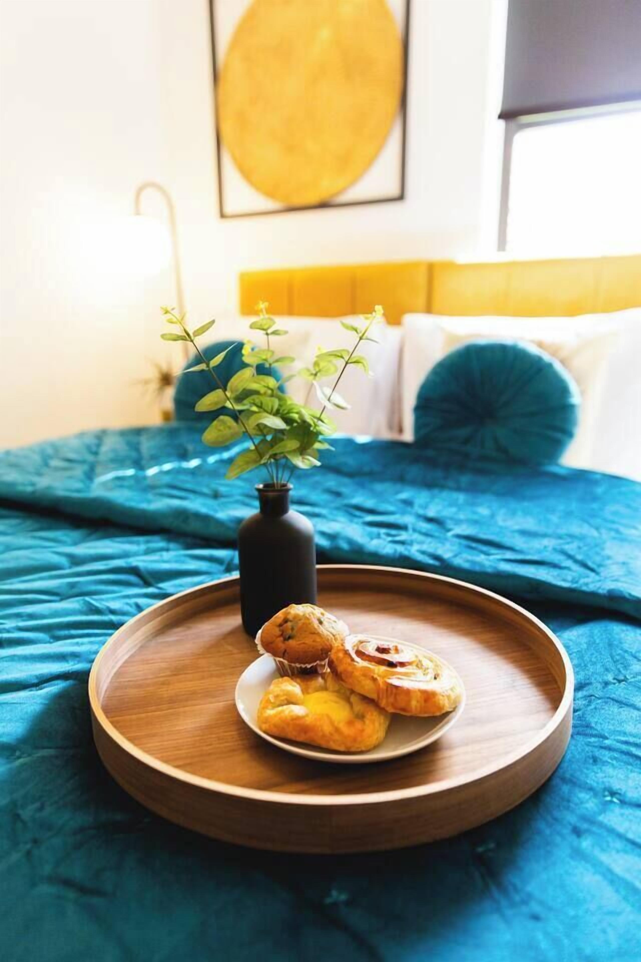 Ein Bett mit blauer Bettdecke und einem hölzernen Tablett mit Gebäck und einer kleinen Pflanze.