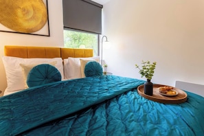 A bed with a teal duvet, white pillows, and a wooden tray with pastries.