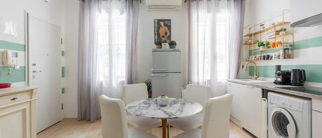A compact kitchen with a built-in washing machine, a dining area with a marble table, and a small refrigerator.