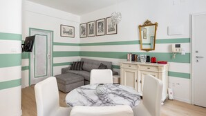 A room with a sofa, a dining table with chairs, a cabinet with books, a mirror, and a door with a lock. - Casa 3 Frecce a Corte Isolani by Wonderful Italy (Bologna)