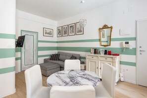 Ein Zimmer mit einer Couch, einem Esstisch mit Stühlen, einem Bücherregal, einem Spiegel und einer Tür mit Schloss.