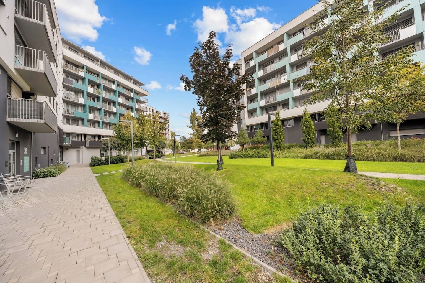 A residential building with multiple balconies, a paved walkway, and a well-maintained grassy area with trees.