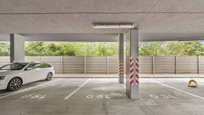 Eine Parkgarage mit Betonpfeilern, ein weißes Auto in einem Stellplatz und eine Metallsperre mit roten und weißen Streifen.
