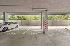 A parking garage with concrete pillars, a white car parked in a designated space, and a metal barrier with red and white stripes. - AC 1 room Apartment, Hranicna street (Bratislava)