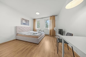 A bedroom with a bed, a desk, a chair, a window with curtains, and a radiator. - AC 1 room Apartment, Hranicna street (Bratislava)