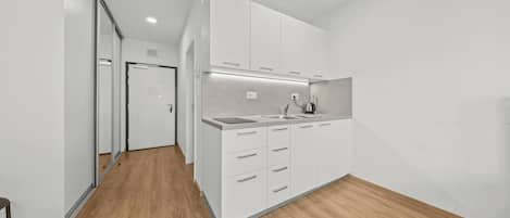A modern kitchen with white cabinetry, a wooden floor, and a recessed ceiling light.