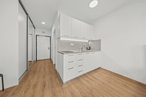 A modern kitchen with white cabinetry, a wooden floor, and a recessed ceiling light. - AC 1 room Apartment, Hranicna street (Bratislava)