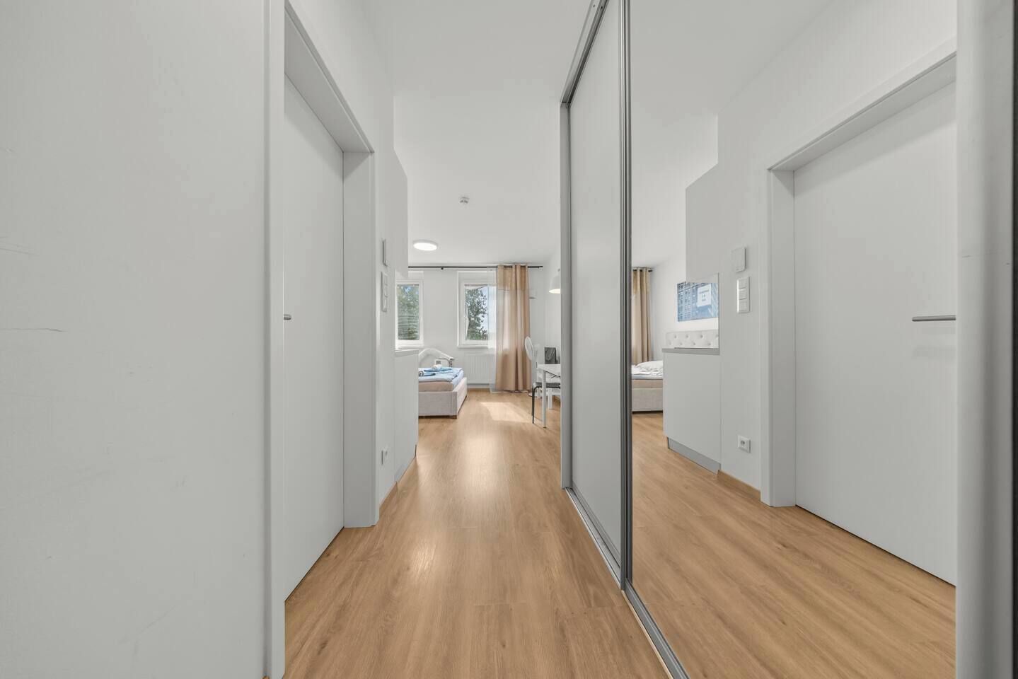 Un corridoio con pavimento in legno che conduce a una camera da letto con un letto, una sedia e una scrivania.