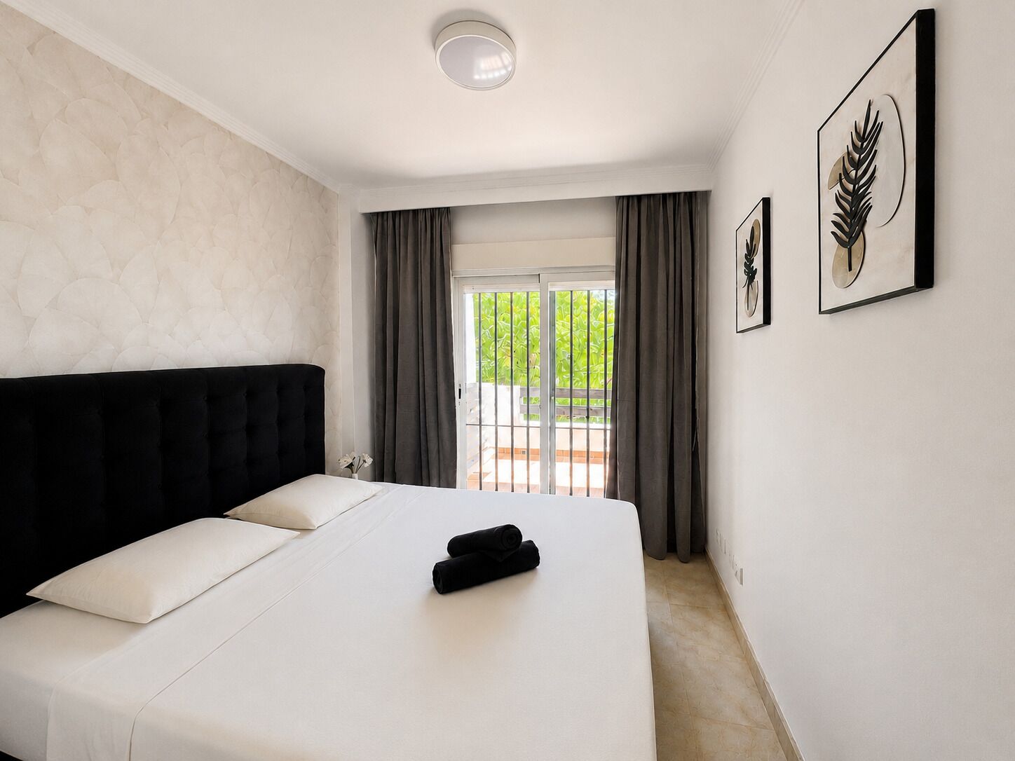 A hotel room with a large bed, a view to the outside, and two framed artworks on the wall.
