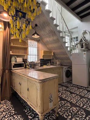 A kitchen with a central island, a washing machine, and a staircase leading to an upper level. - A colorful Bohemian retreat with unique design and cozy vibes. Good location (Chang Wat Chiang Mai)