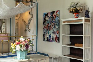 A room with a white vanity, a mirror, a floral arrangement, a colorful abstract painting, and a blue and white shelving unit.