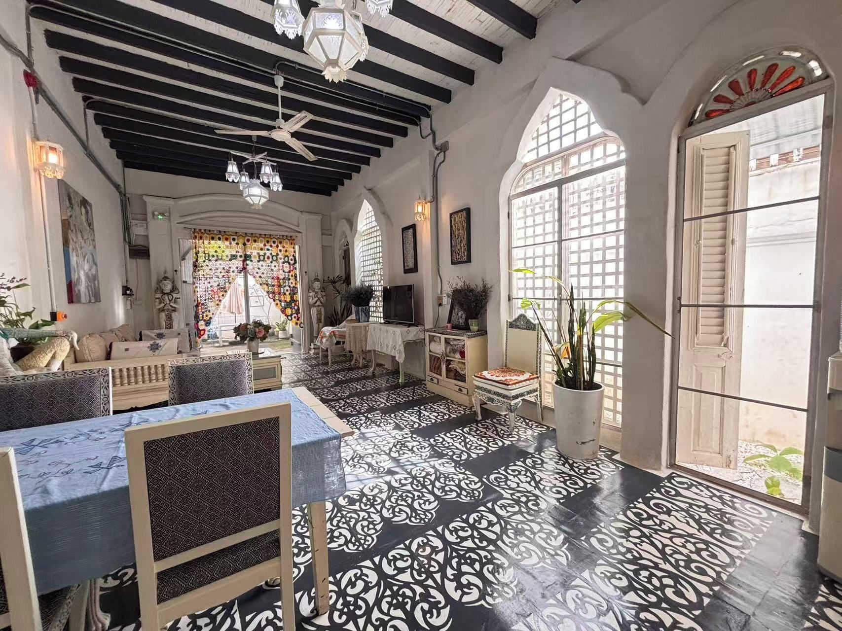 A spacious room with a high ceiling, patterned floor, and a view through a large window.