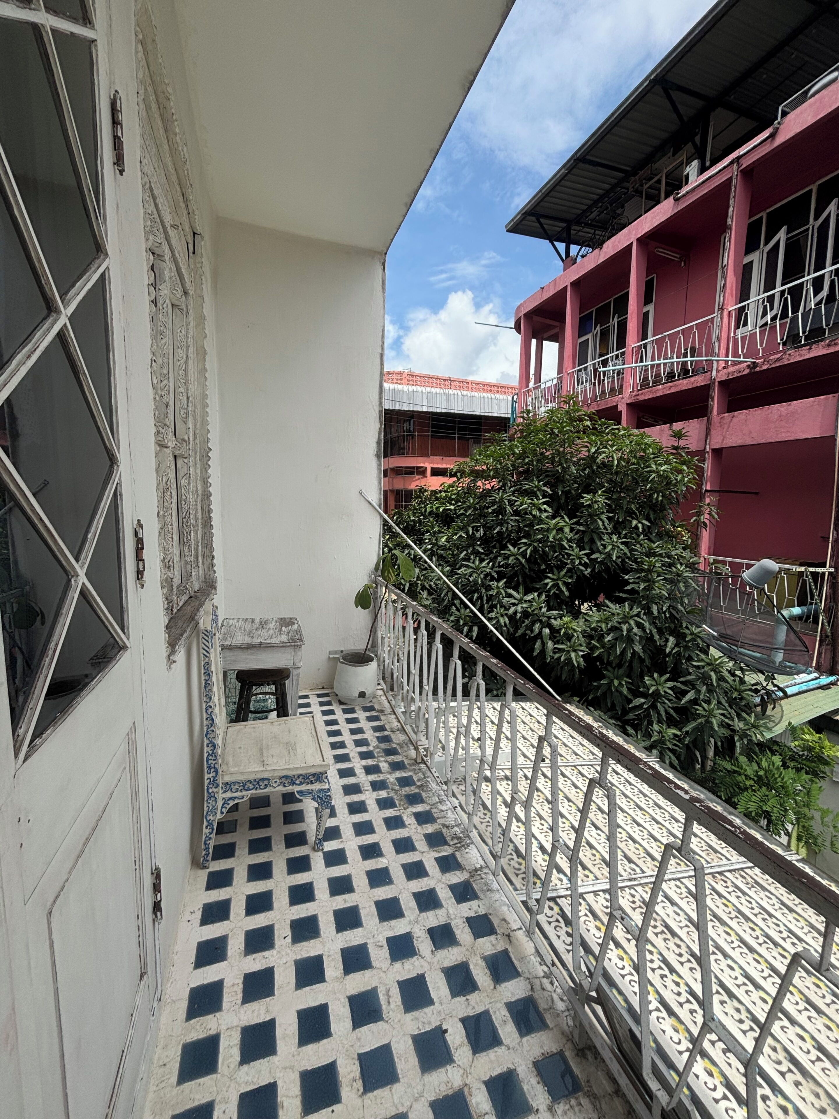 A narrow balcony with a checkered floor, a potted plant, and a metal railing.