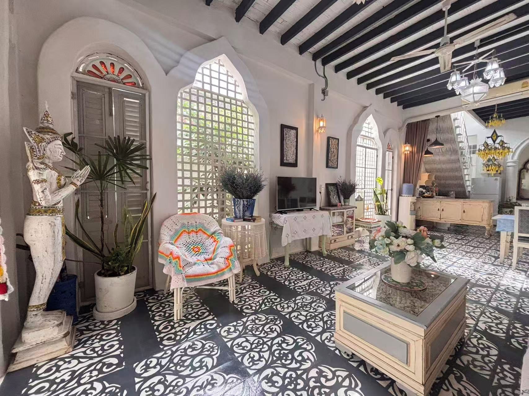 A room with a patterned floor, a statue, a television on a table, and a chandelier.