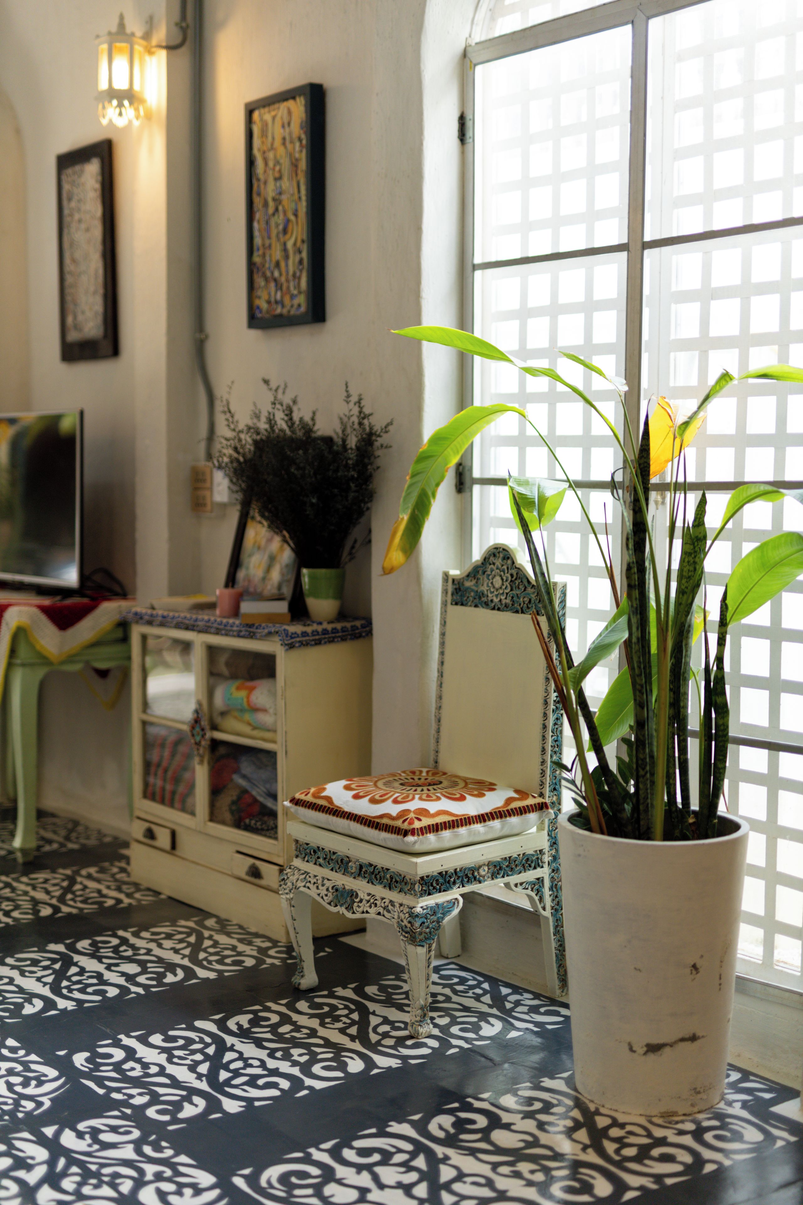 A room with a patterned floor, a potted plant, a decorative chair, and wall-mounted artwork.