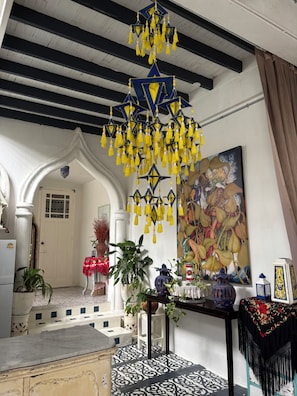A room with a hanging yellow tassel chandelier, a large painting, and a patterned floor. - A colorful Bohemian retreat with unique design and cozy vibes. Good location (Chang Wat Chiang Mai)
