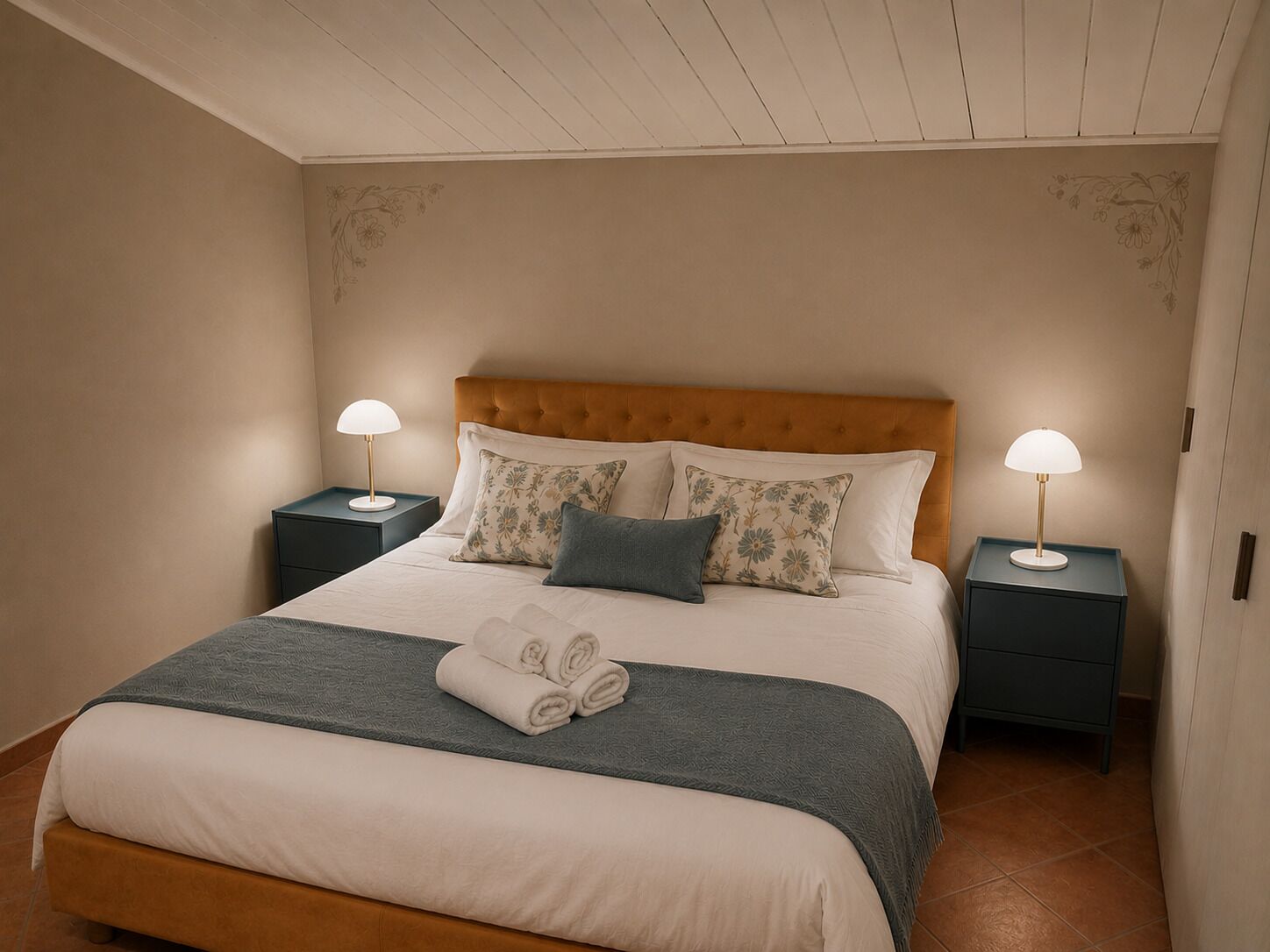 A neatly made bed with a headboard, two bedside tables with lamps, and a folded towel on the bed.