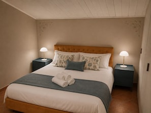 Una cama bien hecha con un cabecero, dos mesitas de noche con lámparas y una toalla doblada sobre la cama.
